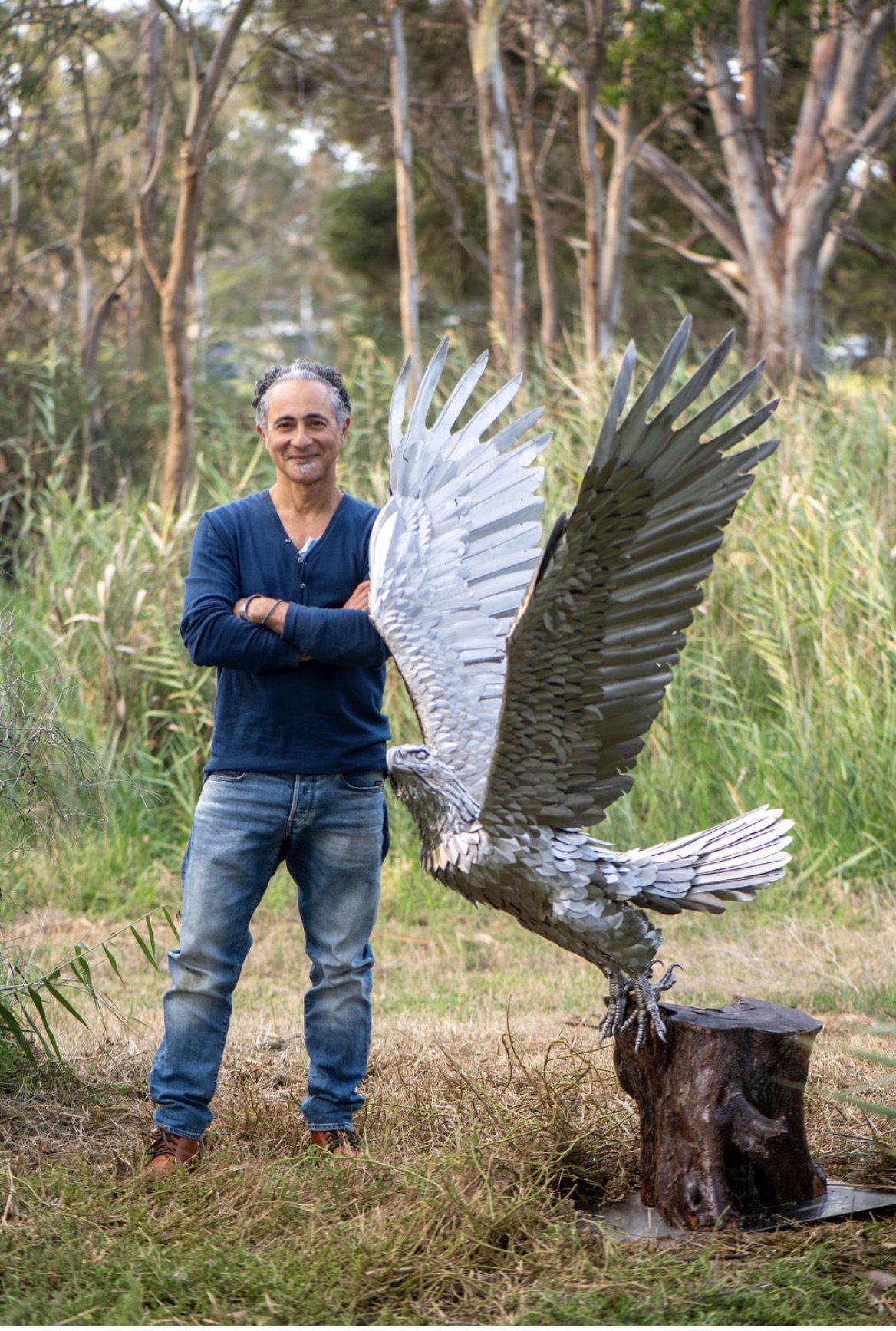 Anmar Alsabiri standing beside his stainless steel eagle sculpture Ascension